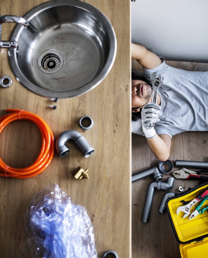 Time To Replace Your Sewer Pipes, man under a sink fixing sewer pipe